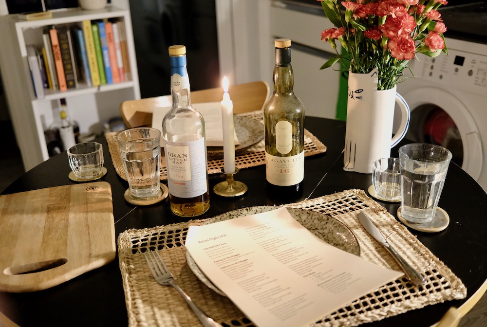 A table laid with candles and bottles of whisky and a programme for Burns Night with songs