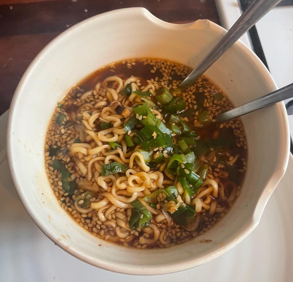 A ramen bowl with broth, noodles, scallions, and seeds