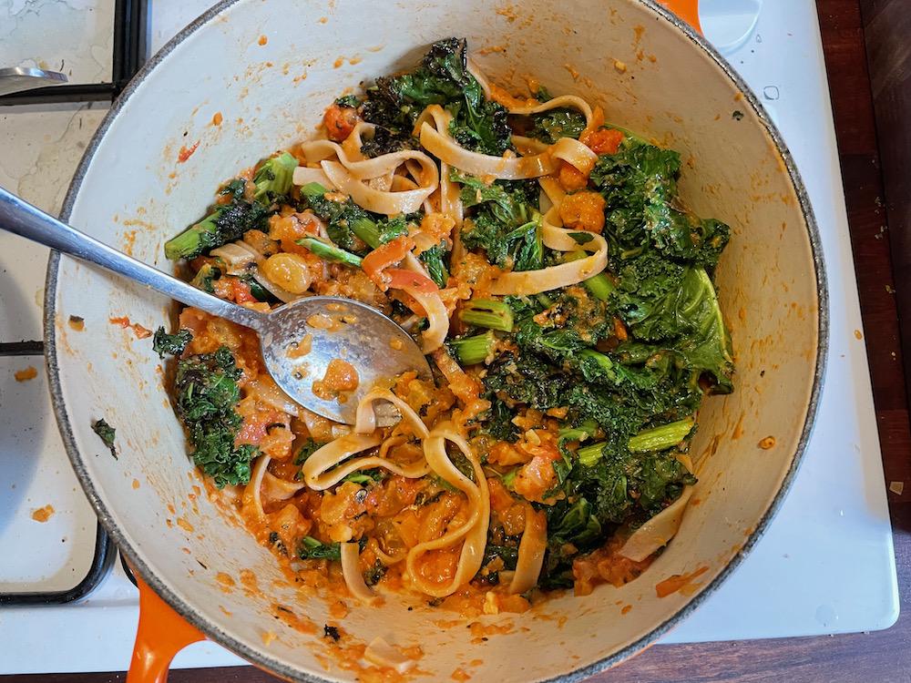 A cooking pot with pasta, kale, and tomato sauce