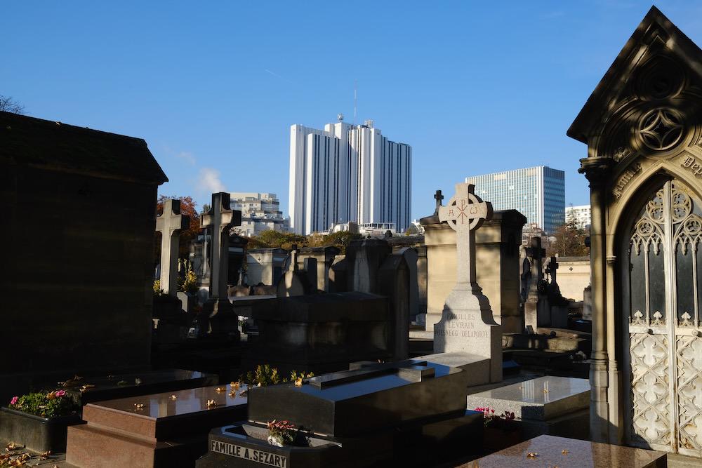 A modern building in the background of a dense, urban graveyard