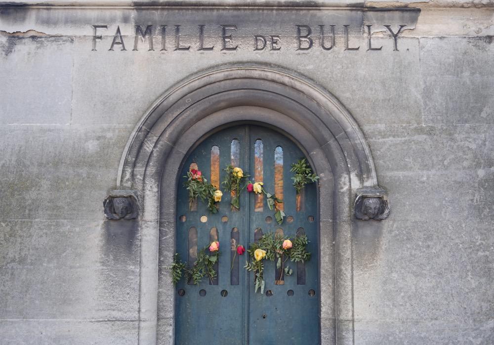 Flowers on the front of a stone mausoleum with an engraved sign for &quot;Famille de Bully&quot;