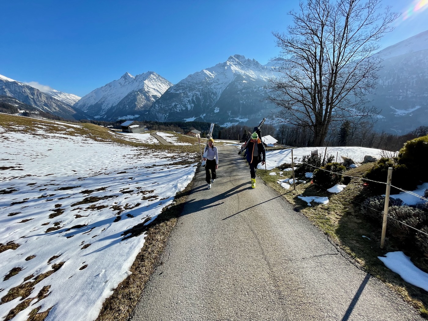 A man and woman climbing a hill with skis over their shoulders