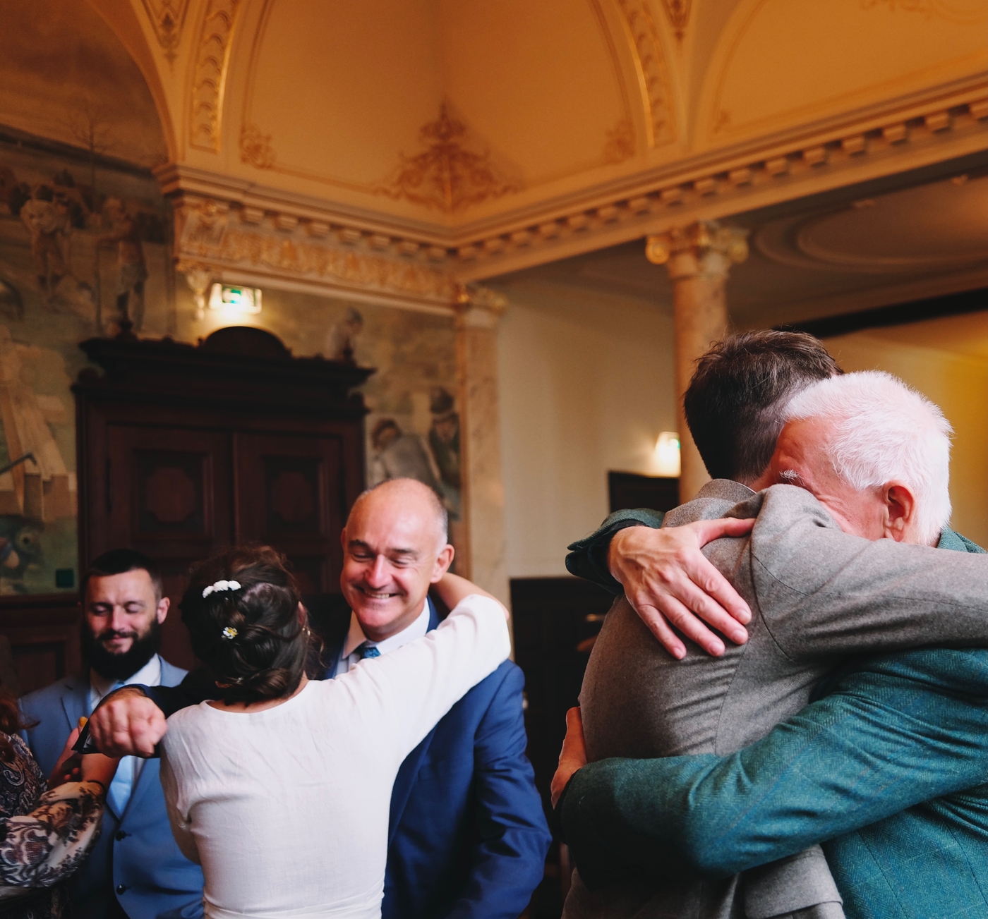A bride and groom hugging two older men in a registry office