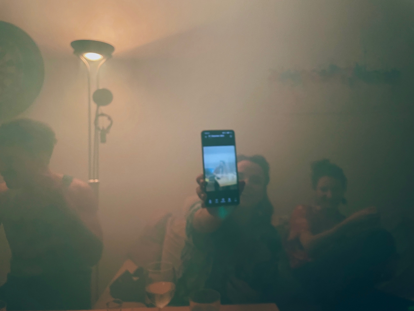 A girl holding up a phone obscured by smoke at a party