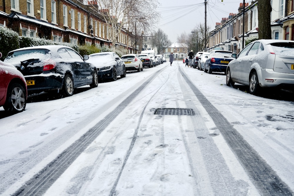 A residential road covered in snow and a family playing in the distance