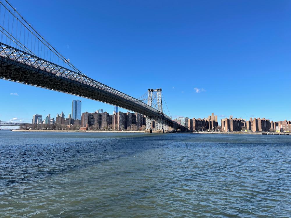 A suspension bridge over a wide river, with project housing on the far bank