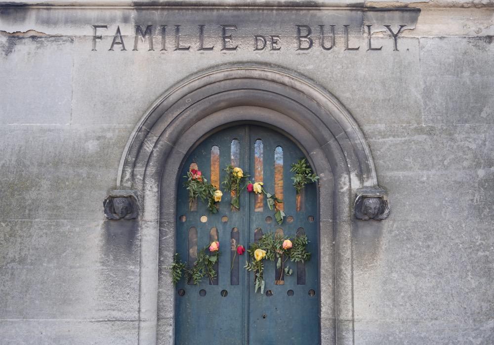 Flowers on the front of a stone mausoleum with an engraved sign for "Famille de Bully"