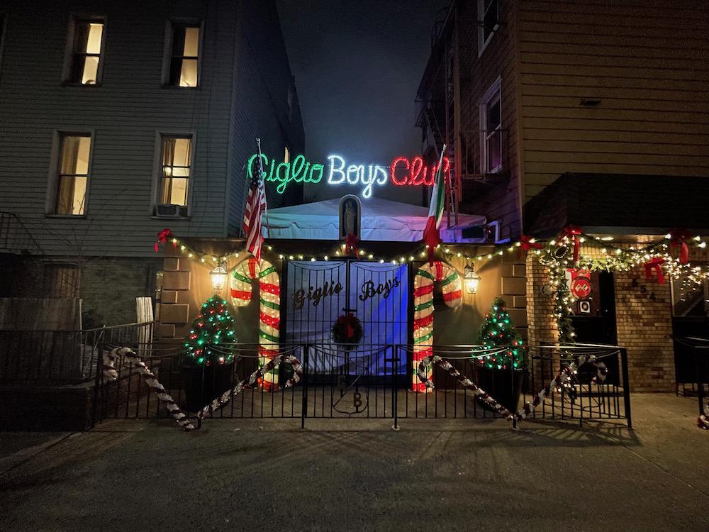 A gate labelled "Giglio Boys Club" covered in illuminated Christmas decorations